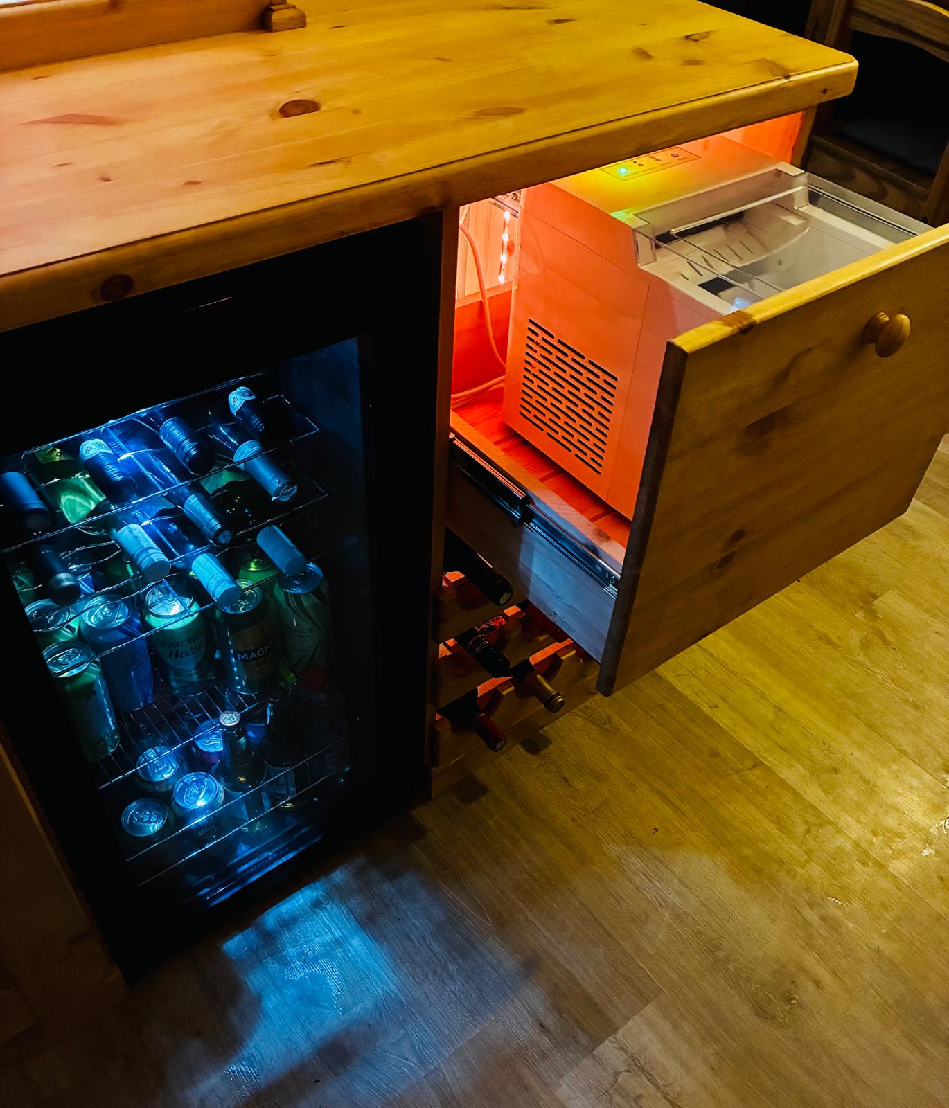 Deep drawer pulled open showing a fitted ice machine with hopper, beside an integrated drinks fridge.