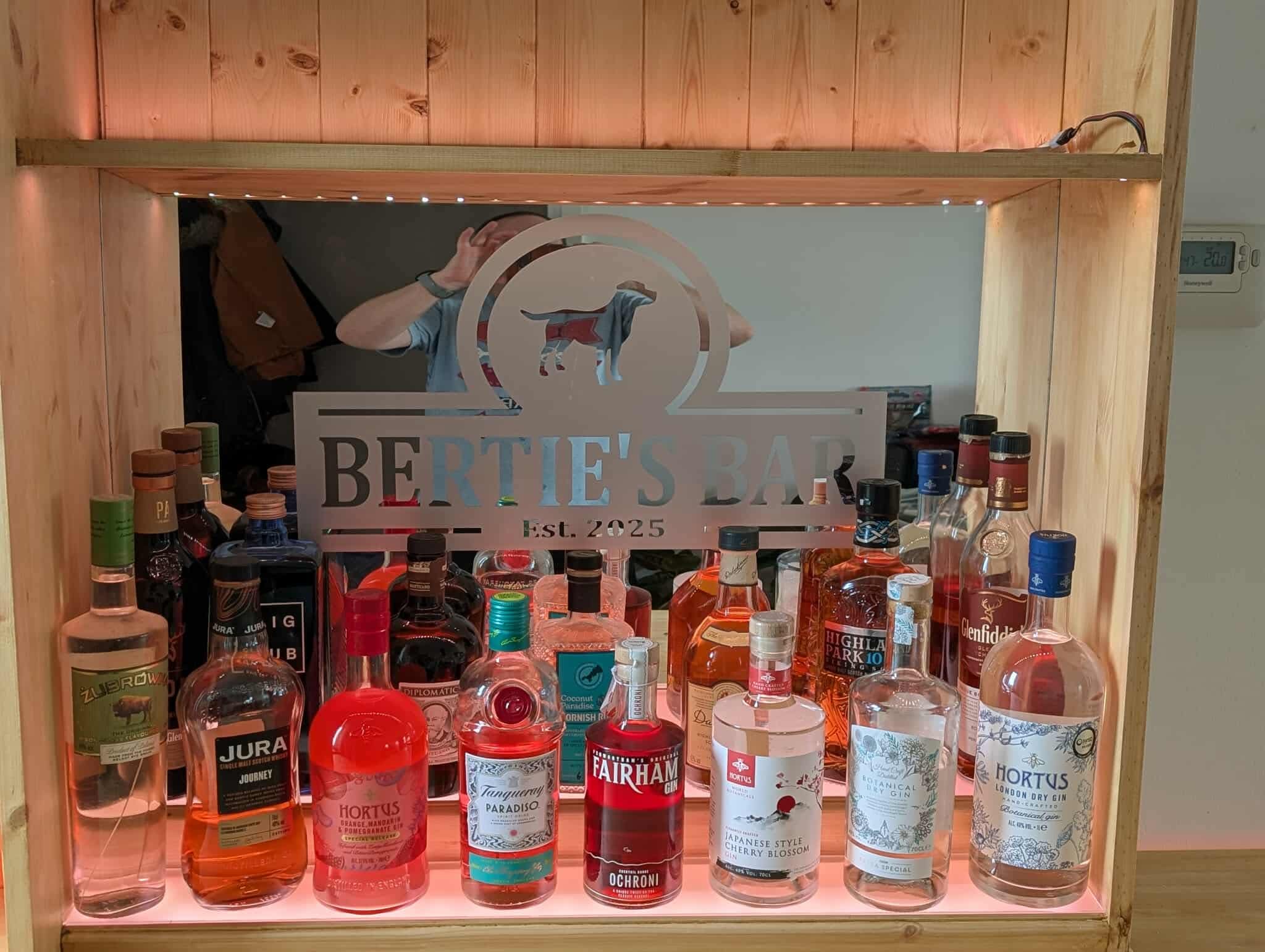 Close-up of the personalised back-bar mirror reading 'Bertie's Bar · Est. 2025' with bottles ranged below.