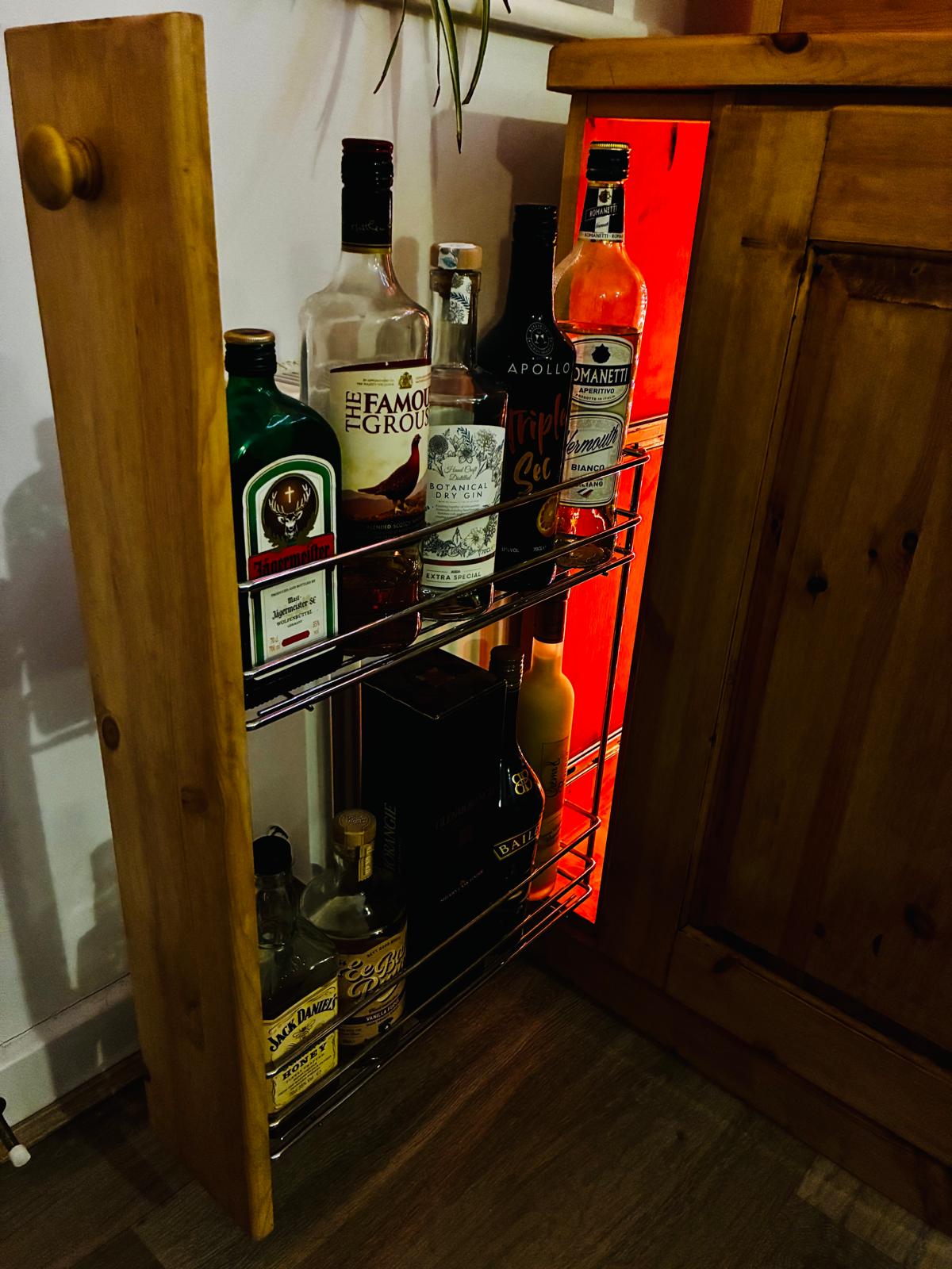 Slide-out spirit drawer pulled open, with bottles standing on a wire rack and an LED glow behind.