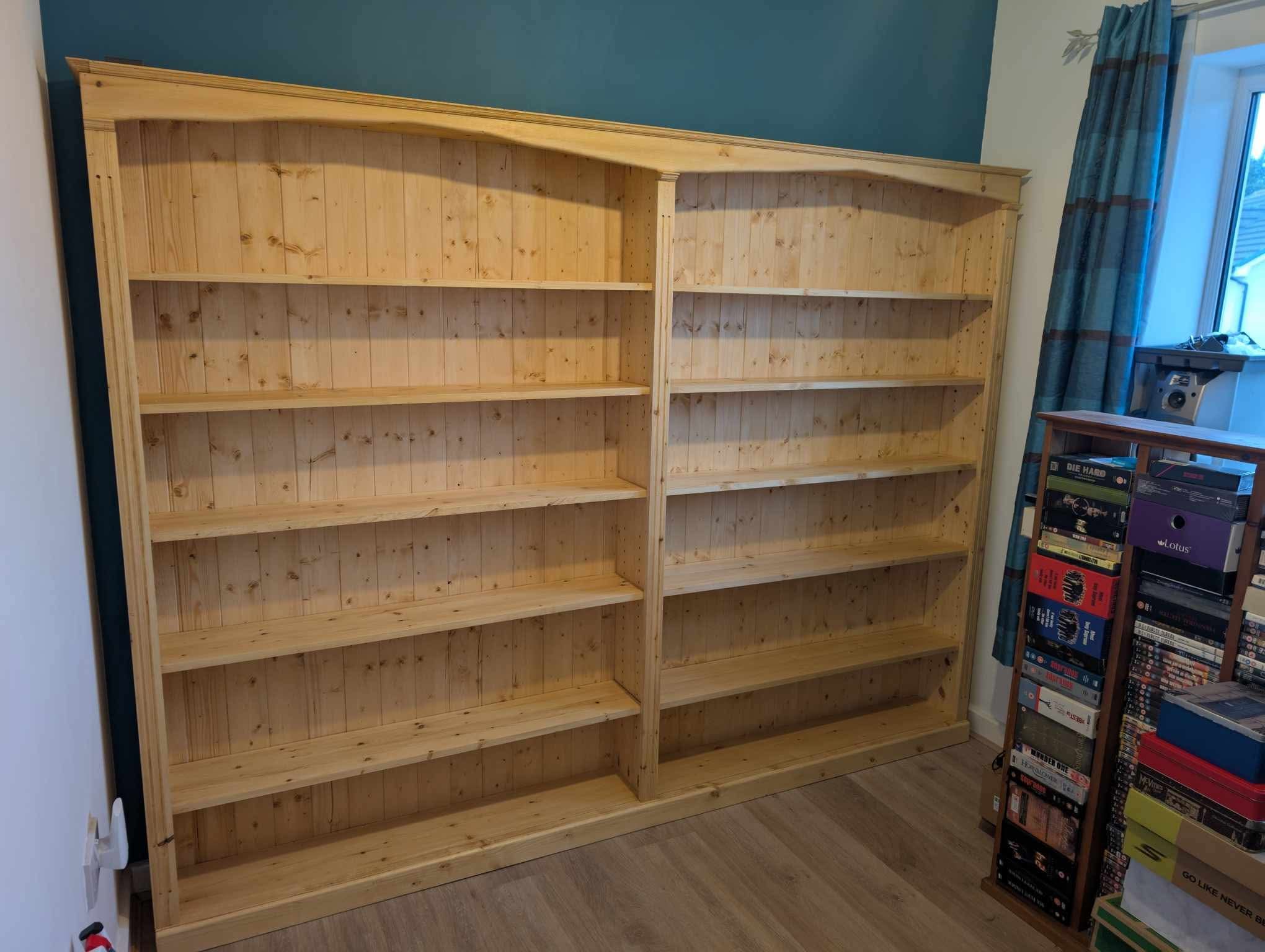 The Buckland Bookcase installed in the room, shelves filled, with daylight through the curtain and another piece of furniture beside it.