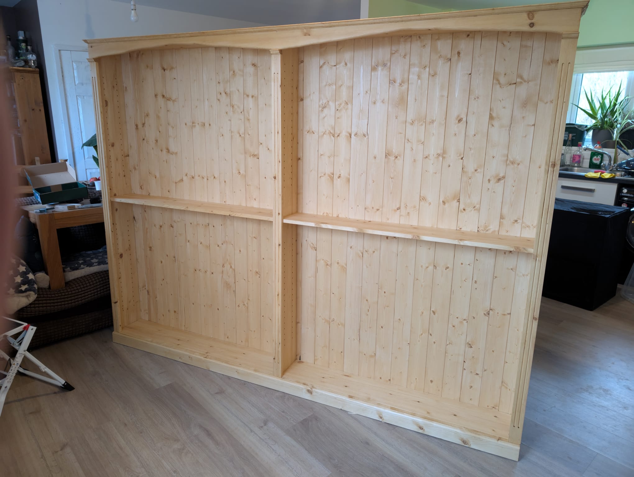 The bookcase mid-build, fully assembled but with shelves not yet in — showing the two bays divided by a centre upright and the fixed middle shelf in each side.