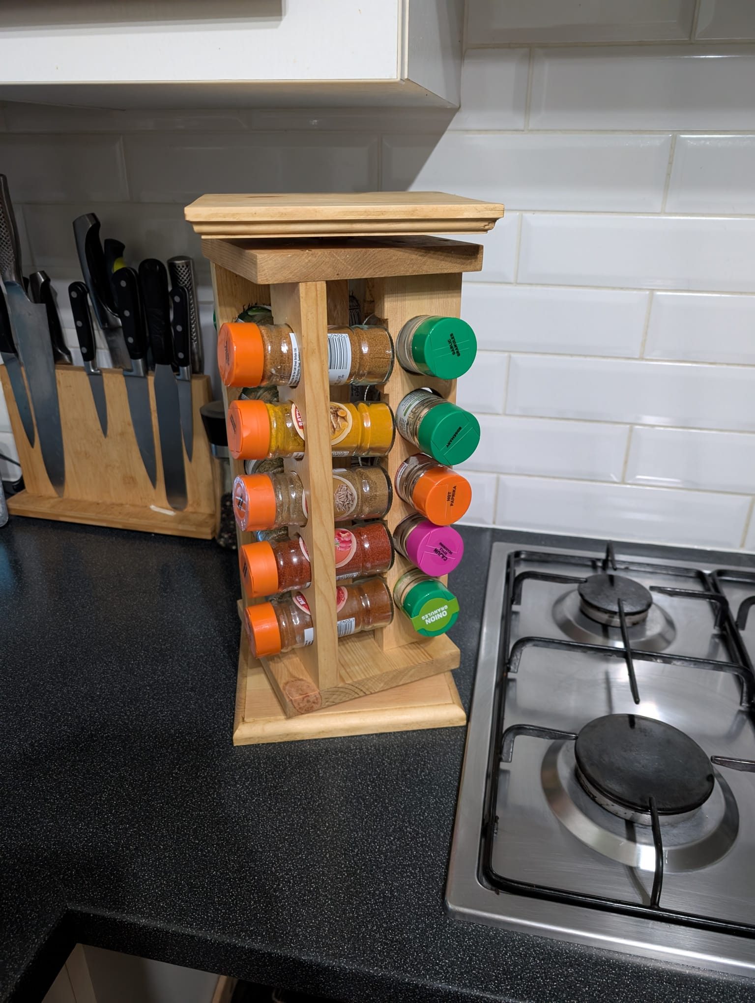 Three-quarter view of the herb carousel showing two faces of jars and the lipped wooden lid on top.